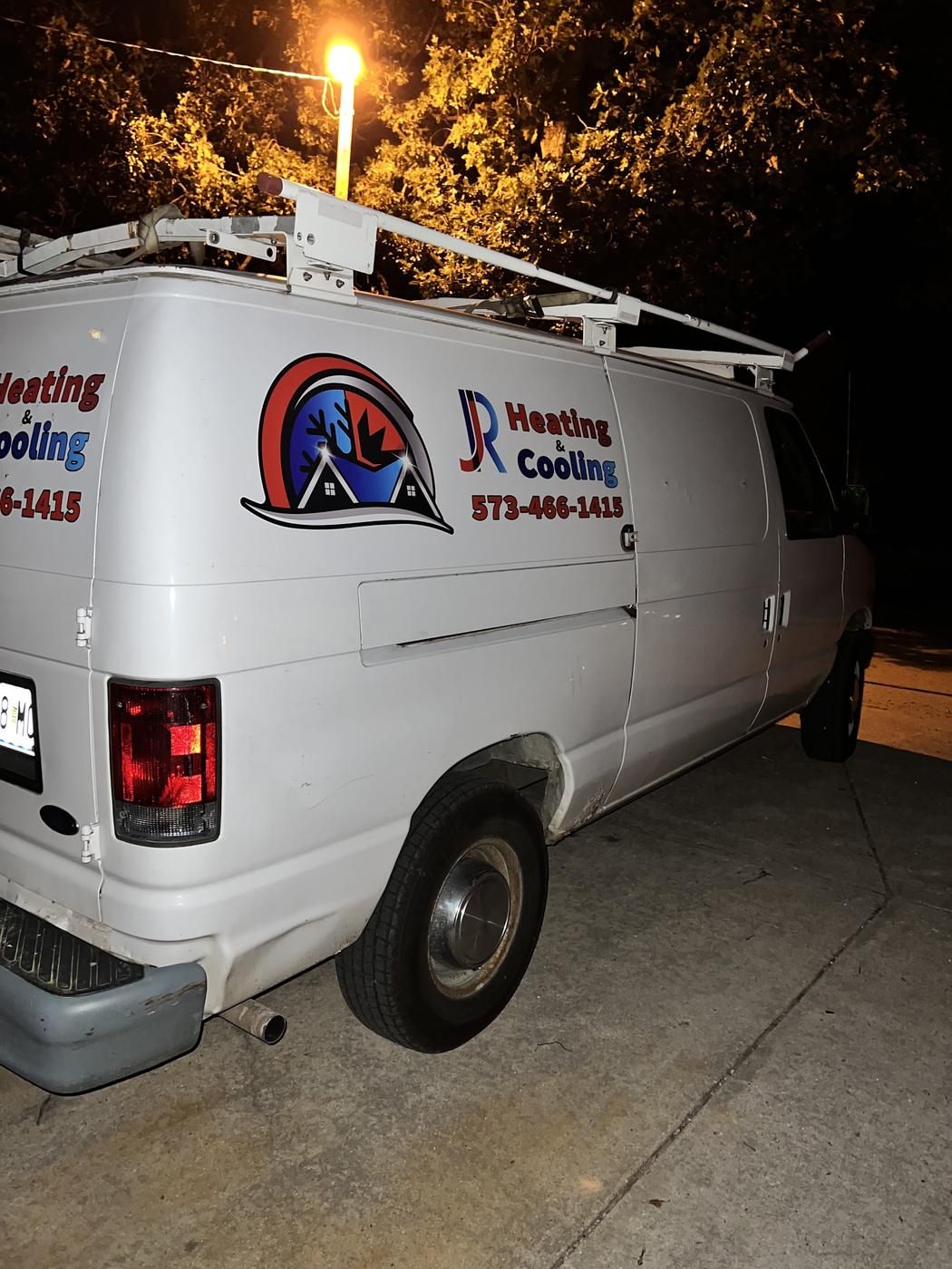 The white J.R Heating & Cooling work van with the logo on the side, parked at night